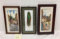 Three framed artworks displayed side by side including two South American village watercolors and one painted feather parrot art.