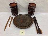 Overview of the set showing two stacks of wooden bowls, a large carved wooden plate in center, and three carved wooden utensils including fork, spoon, and a flat tool.