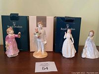 All four Royal Doulton figurines displayed with three original boxes visible behind them on wooden surface.