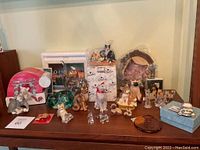Overview of the cat figurines and collectibles displayed on a wooden surface, showing various styles and materials including porcelain, glass, and decorative items.