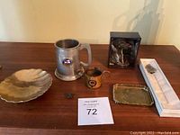 Overview of lot items on wooden surface including stein, brass mug, pin dish, small tray, pins, and boxed figure
