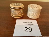 Two cylindrical boxes displayed side by side on wooden surface with auction tag