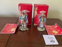 Both Bunnykin figurines with their original red boxes and certificates laid out on a table. Figurines still in clear plastic wrapping.