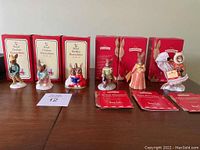 Six Bunnykins Royal Doulton porcelain figurines displayed with their original red and cream boxes behind them on a wooden surface.