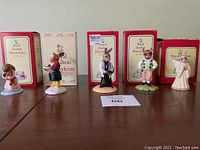 Front view of all five Bunnykins figurines lined up next to their original boxes on a table.