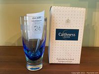 Blue glass vase standing next to its original box with a note inside the vase.