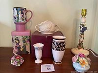 Group shot showing various floral ceramic and porcelain pieces including vase, lamp base, floral arrangements, and boxed thermal mug