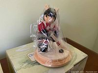 Photo of a Royal Doulton Bunnykins hockey figurine, still wrapped in plastic, standing on a round wooden base and sitting on its original box.