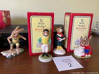 Four Royal Doulton Bunnykins ceramic figurines including a surfer, jockey, collector bunny, and a pair reading a book, two with original boxes.