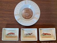 Top view of the Royal Doulton ashtray with Winston Churchill portrait and three small hand-painted dishes featuring foxes and a hound, arranged on wood surface.