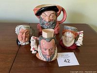 Four Royal Doulton toby jugs displayed on a table, showing character heads including Falstaff and others.