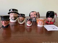 Front view of 7 Royal Doulton Toby jugs and mugs in mini and small sizes displayed on wooden surface.