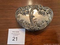 Closed view of silver plate jewelry box shaped like double entwined hearts with floral embossed design on top
