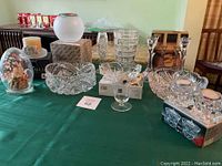 Wide view of crystal and glass lot on green tablecloth showing various bowls, candle holders, vases, and decorative dome.