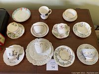 All vintage cups and saucers, including one trio with under plate, a family crest mug, odd saucer, and finger bowl arranged on wood surface.
