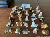 Photo showing 30 small ceramic animal figurines including pigs, foxes, dogs, owl, turtle, and butterfly laid out on a wooden surface.