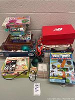 Front view of stacked vintage board games, puzzle sets, a green adjustable table lamp, and a BTS matching card game. Visible games include Angry Birds themed game, Pachisi, and Dinosaurs and Prehistorics Lotto.