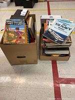 Two large boxes containing assorted vintage books and magazines with various covers including war history and illustrated children's books.