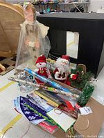 Photo showing assorted holiday decorations on black table including snowman and Santa dolls, holiday basket, wrapping paper, and LED tree decoration.