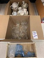 Open box with porcelain dishes including teapot, cups, and saucers, visible porcelain bird figurine and salt and pepper shakers.