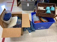 Box and bin containing multiple plastic containers, dishes, and other kitchen items on floor.