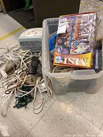 Photo of the lot showing a plastic bin containing the boxed TV Anywhere Plus system, assorted cords, a small fan, and power bars scattered around the bin, along with string lights on the floor.