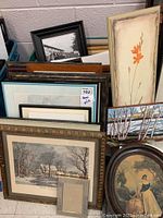 Various framed prints stacked including flower art and black and white photo