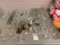 Full view of the wide assortment of glassware including clear stemmed glasses, clear tumblers, decorative glass pieces, and various colored glasses on a table.