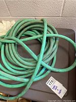 Coiled green garden hose placed on top of plastic hose reel storage box
