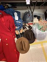 Overview of red wool coat, rolled vintage wool blanket, two pairs of women's sandals, and two brown leather suede cowboy hats on floor near bags