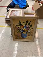 Five framed artworks stacked with one prominently showing textured oil painting of flowers in a blue vase.