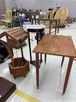 Photo showing three wood tables including a wishing well, three-leg stone top table, and rectangular wood side table in a warehouse.