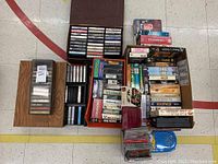 Wide shot of VHS tapes, cassette tapes in holders, CDs, and other media items spread on floor and small table