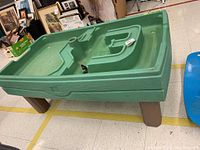 Green kids water table with brown legs seen at an angle on tiled floor indoors