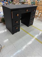 Black painted wooden desk with drawers on each side and center. Scratches visible. Rounded knobs.