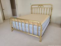 Full view of queen-size bed with brass headboard and footboard, mattress, and boxspring in a room with carpeted floor.