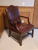 Side angle showing dark brown leather upholstery, wooden frame, and nailhead trim on chair edges.