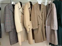 Five men's coats hanging in a row showing color and styles including beige, tan, and checkered coats