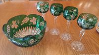 Full view of crystal fruit bowl and four goblets on a wooden table showing the detailed cut to clear floral and grape patterns.
