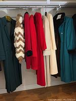 Eight ladies winter coats hanging on rack showing various colors and materials including cashmere, wool and fur lining.