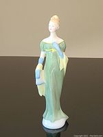 Front view of Royal Doulton Lorna figurine in green dress holding yellow shawl with blue gloves and hair ribbon.