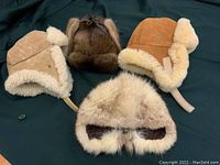 Four winter hats shown together including one full fur pull-on style and three trapper style hats with mink fur and shearling with suede exterior.