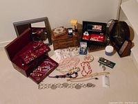 Overview photo of the jewellery lot showing boxes, necklaces, bracelets, earrings, watches, powder compact, cologne sprayer, cleaner jar, and mirrors.