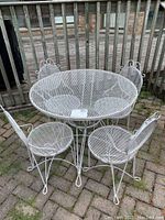 Full view of white metal round patio table and four matching chairs
