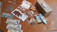 Photo of entire collection of Canadian and USA coins, bills, and metal cash box on wooden surface.