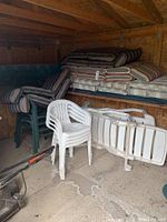 Stacked plastic patio chairs, including white and dark green chairs, plastic lounge chairs folded, and striped chair cushions stacked on shelves.