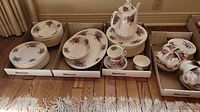 Wide shot of stacked plates, bowls, cups, saucers, teapot and sugar bowl in MaxSold boxes