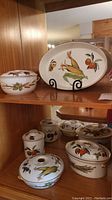 Display of the five piece Evesham set on wooden shelving with colorful vegetable and fruit decoration and gold trim.