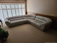 Full view of L-shaped beige sectional sofa against wall with shutters