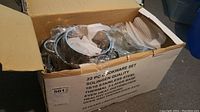 Open cardboard box with multiple plastic-wrapped stainless steel pots and lids